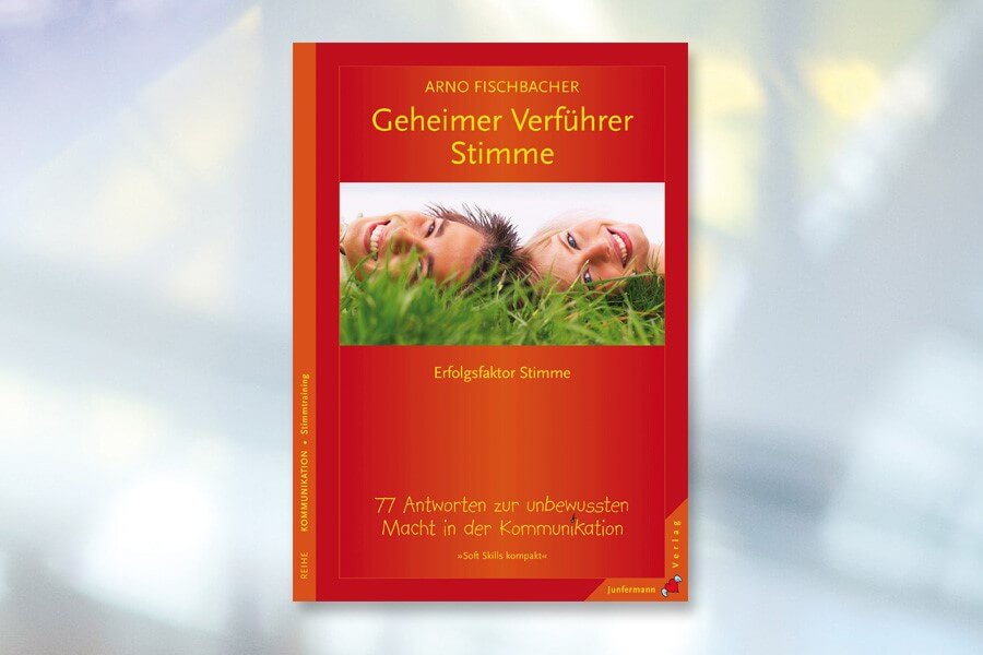 Buchcover von „Geheimer Verführer: Stimme“ von Arno Fischbacher, auf dem zwei lächelnde Menschen im Gras liegen, mit einem Text, der die Kommunikationskraft der Stimme beschreibt.