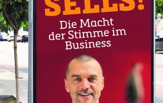 Werbeplakat an einer Straße mit dem Buch „Voice Sells! Die Macht der Stimme im Business“ von Arno Fischbacher, seinem Portrait und begleitenden Presseinformationen.