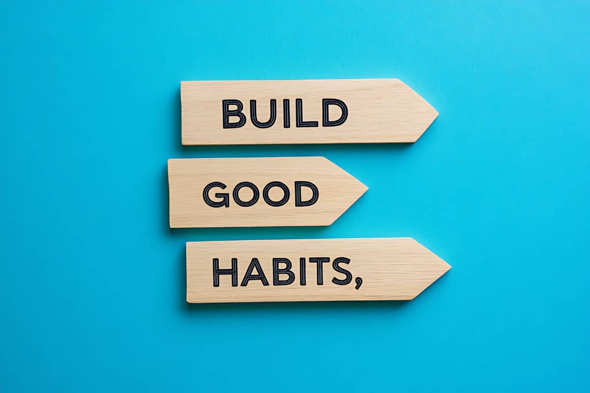 Drei hölzerne Pfeile auf blauem Hintergrund zeigen die Worte "BUILD GOOD HABITS", jedes Wort auf einem eigenen Pfeil, vertikal angeordnet - perfekt, um alte Muster zu durchbrechen und aus dem Autopiloten auszusteigen.